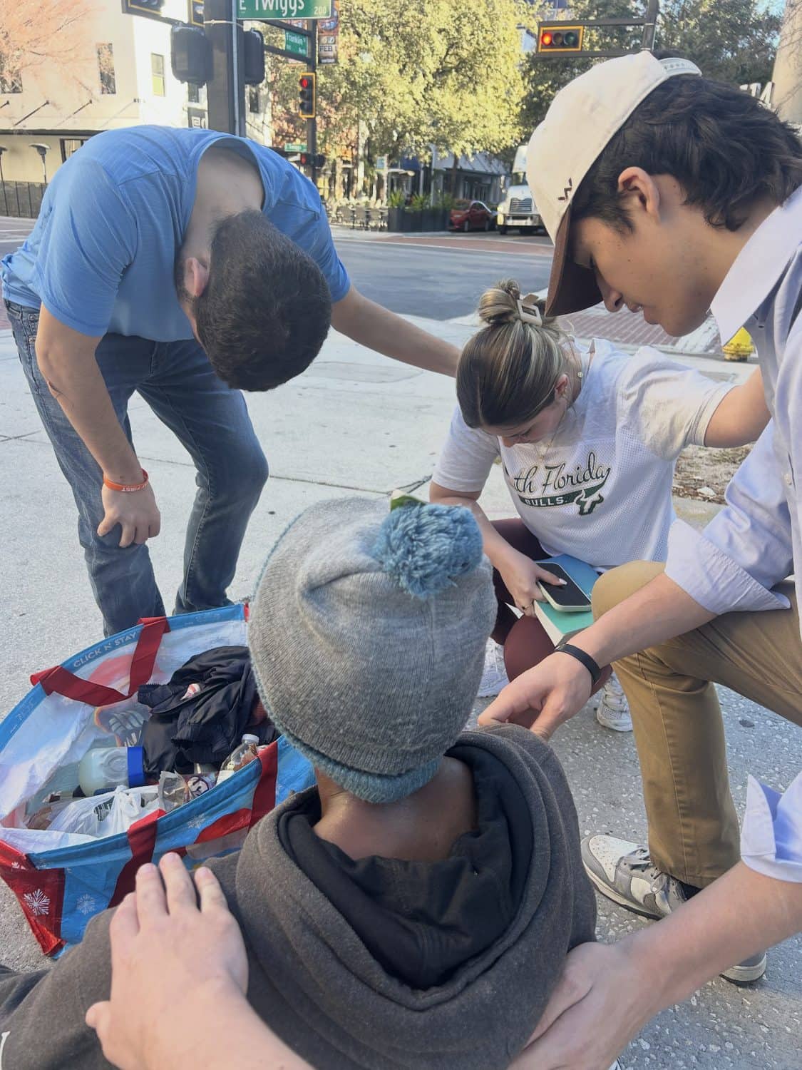 Volunteers kneeling with a man on a downtown Tampa sidewalk, one of them holding his shoulder
